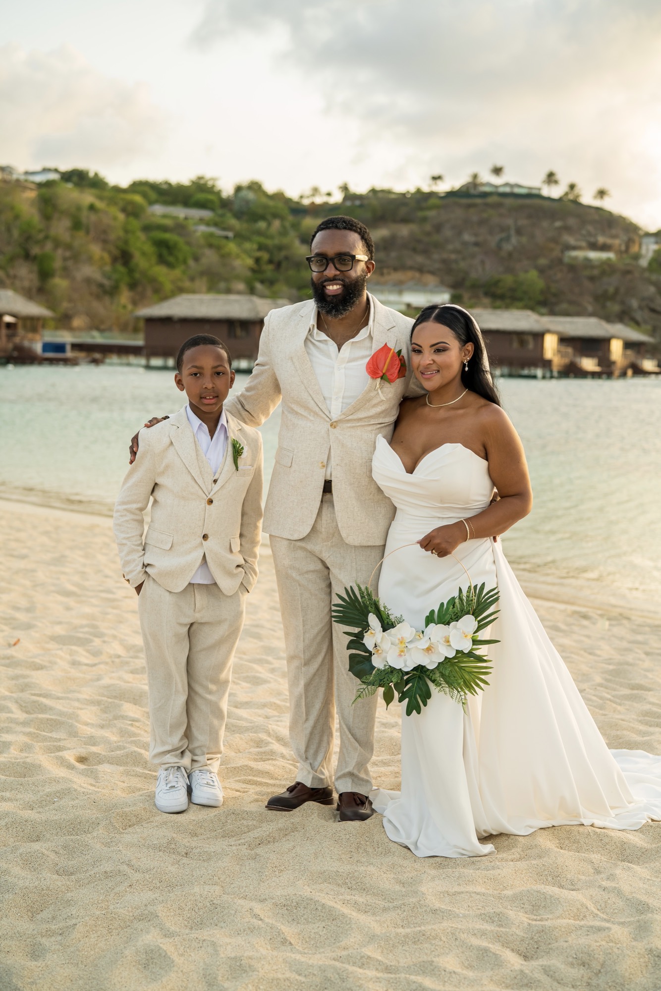 A bride and groom on a beach with two guests in cream suits