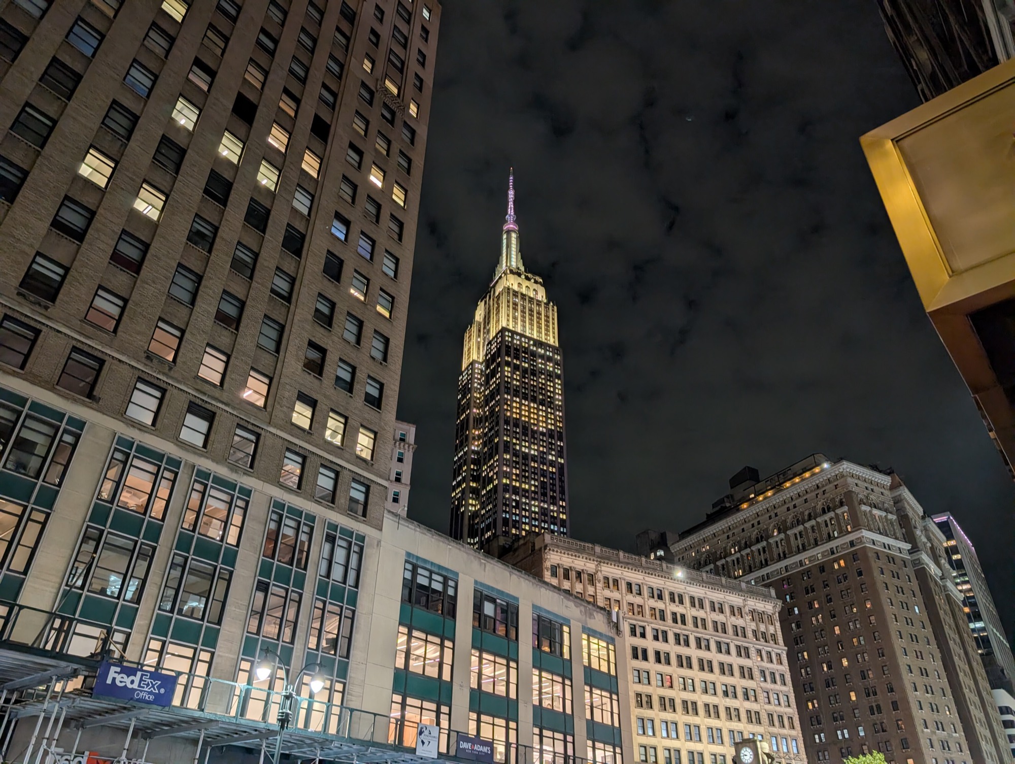 The Empire State Building lit up at night between Midtown towers