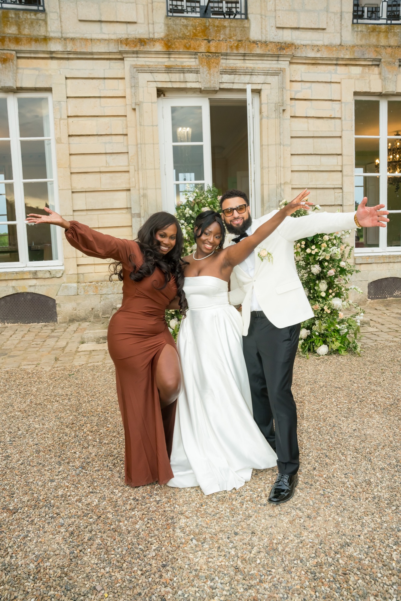 A bride and two guests laughing in a courtyard, arms thrown wide